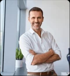 Confident business owner smiling with folded arms near office window